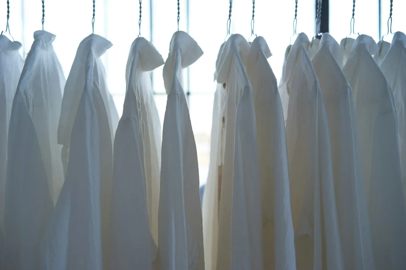 A rail of freshly cleaned white shirts backlit by a window